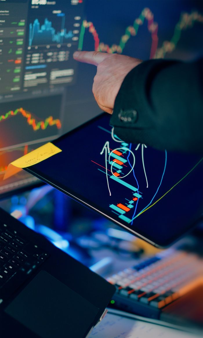 why-choose-us-03 A business professional examines financial charts on a tablet and monitor for investment strategy.