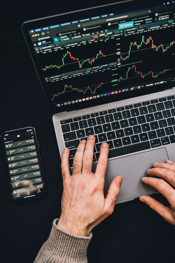 services-01 Hands typing on a laptop with cryptocurrency charts and smartphone display in view, focusing on digital finance.