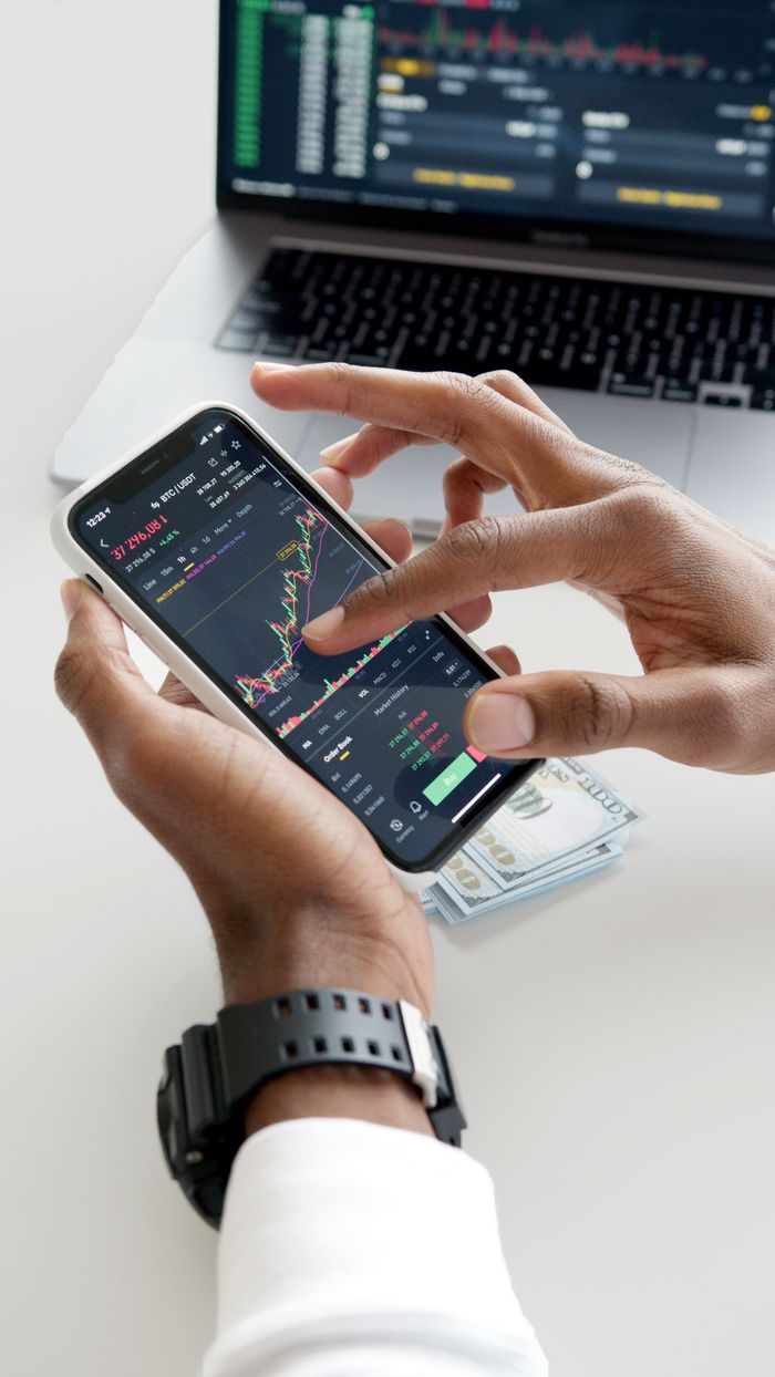 about-02 Hands using smartphone trading app with charts, dollar bills in background.